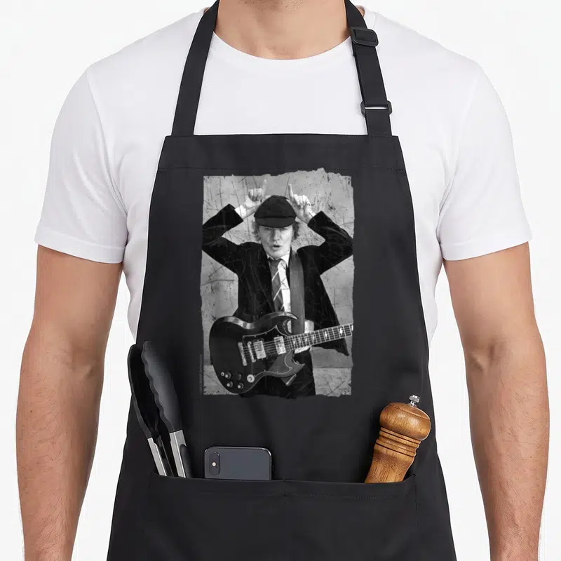 Rock distressed apron - Grayscale photo of man in suit holding guitar and making horn signs on distressed background — shown on a black cotton canvas apron against a white background