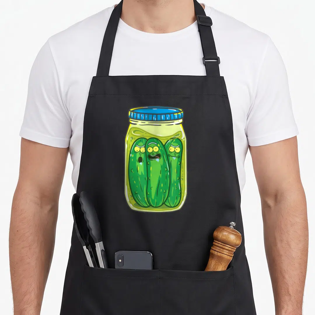 Rick pickle apron - Three green anthropomorphic pickles with faces inside a glass jar with a blue lid in cartoon style — shown on a black cotton canvas apron against a white background