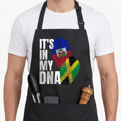 Jamaican haitian heritage aprons - Stacked white text next to two fingerprints filled with Haitian and Jamaican flag — shown on a black cotton canvas apron against a white background