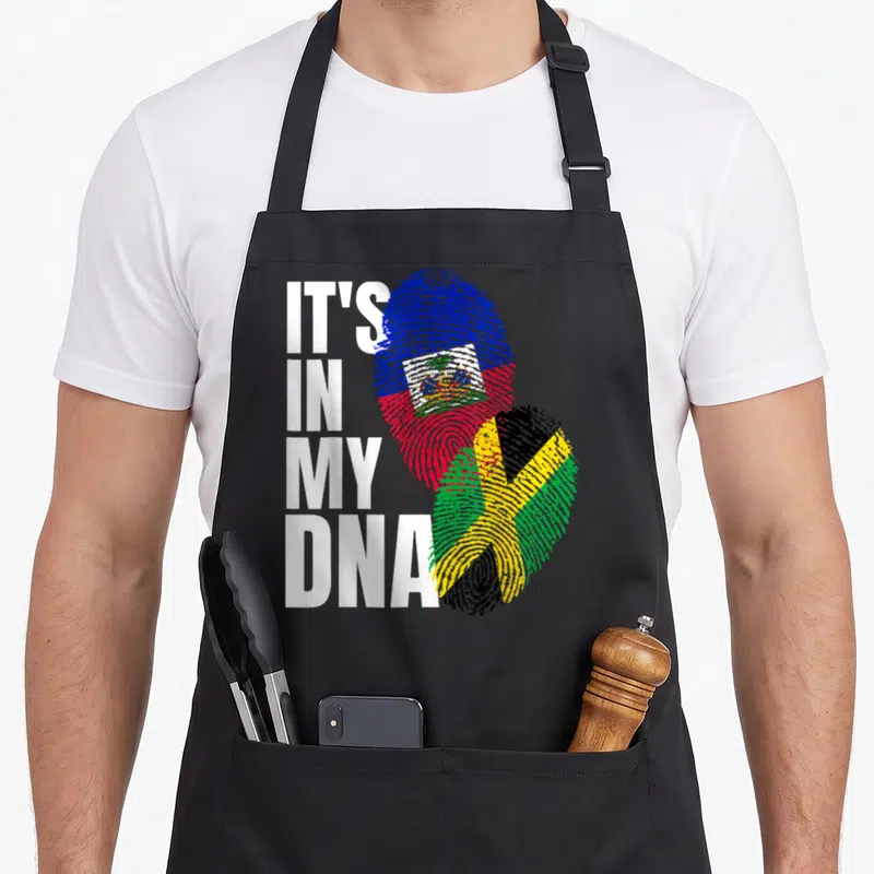 Jamaican haitian heritage aprons - Stacked white text next to two fingerprints filled with Haitian and Jamaican flag — shown on a black cotton canvas apron against a white background