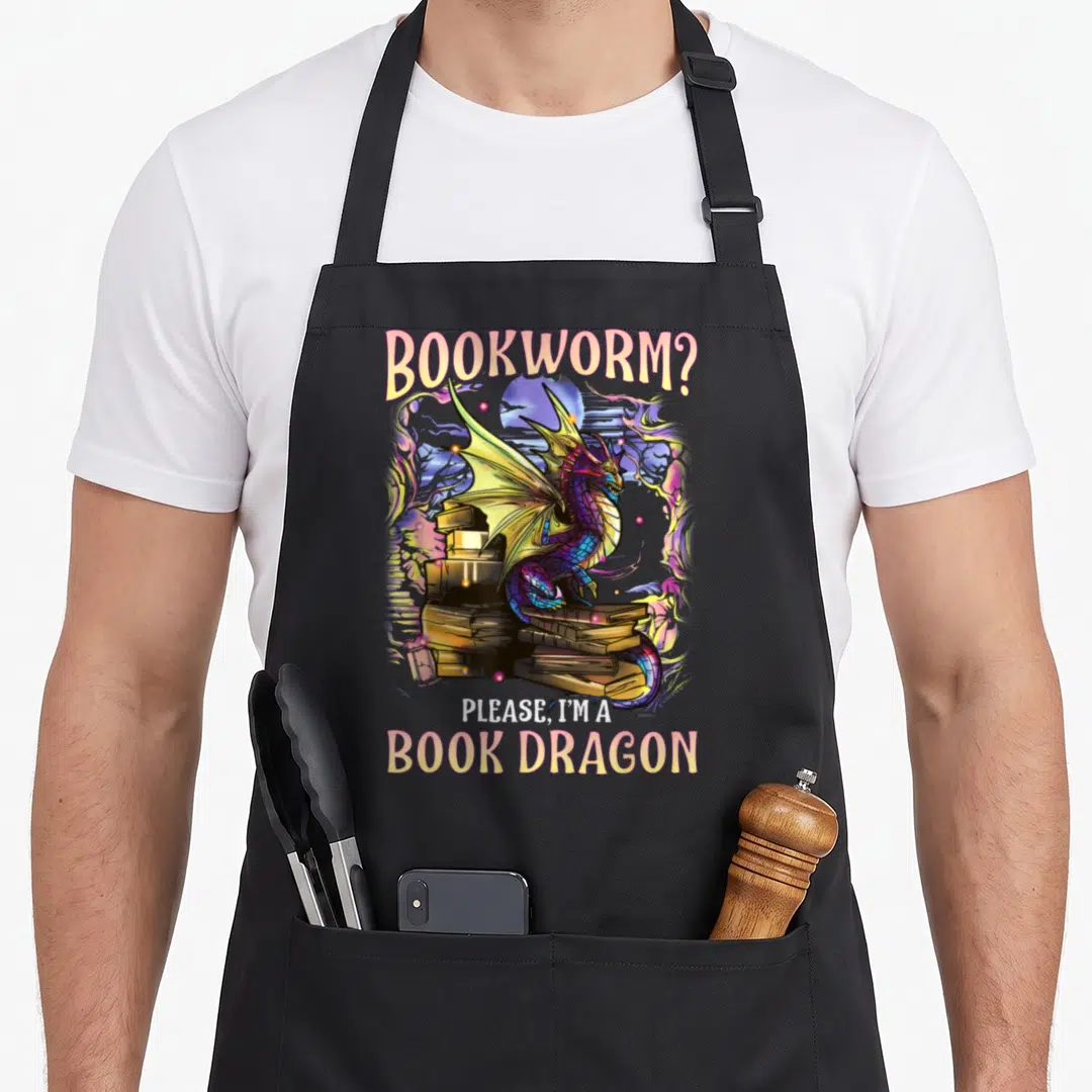 Literacy dragon apron - Cartoon dragon perched on books with text Bookworm Please Im A Book Dragon — shown on a black cotton canvas apron against a white background