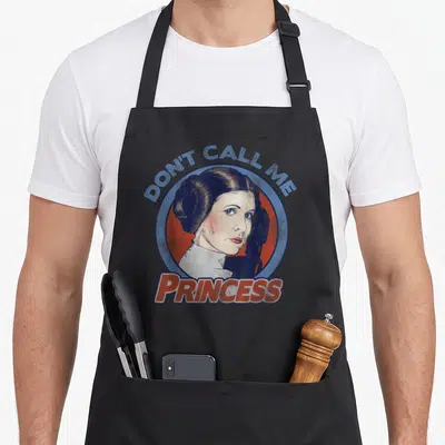 Leia princess apron - Distressed woman portrait inside blue red circle with Don't Call Me Princess text — shown on a black cotton canvas apron against a white background