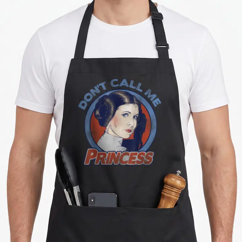 Leia princess apron - Distressed woman portrait inside blue red circle with Don't Call Me Princess text — shown on a black cotton canvas apron against a white background