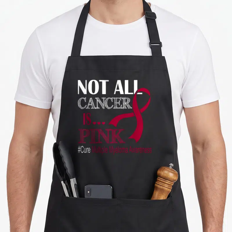 Cancer myeloma awareness apron - Stacked text NOT ALL CANCER IS PINK with red ribbon and three hearts on black bib — shown on a black cotton canvas apron against a white background