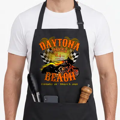 Week bike apron - Retro Daytona 2025 motorcycle graphic with orange lettering, checkered flag, and yellow flames — shown on a black cotton canvas apron against a white background