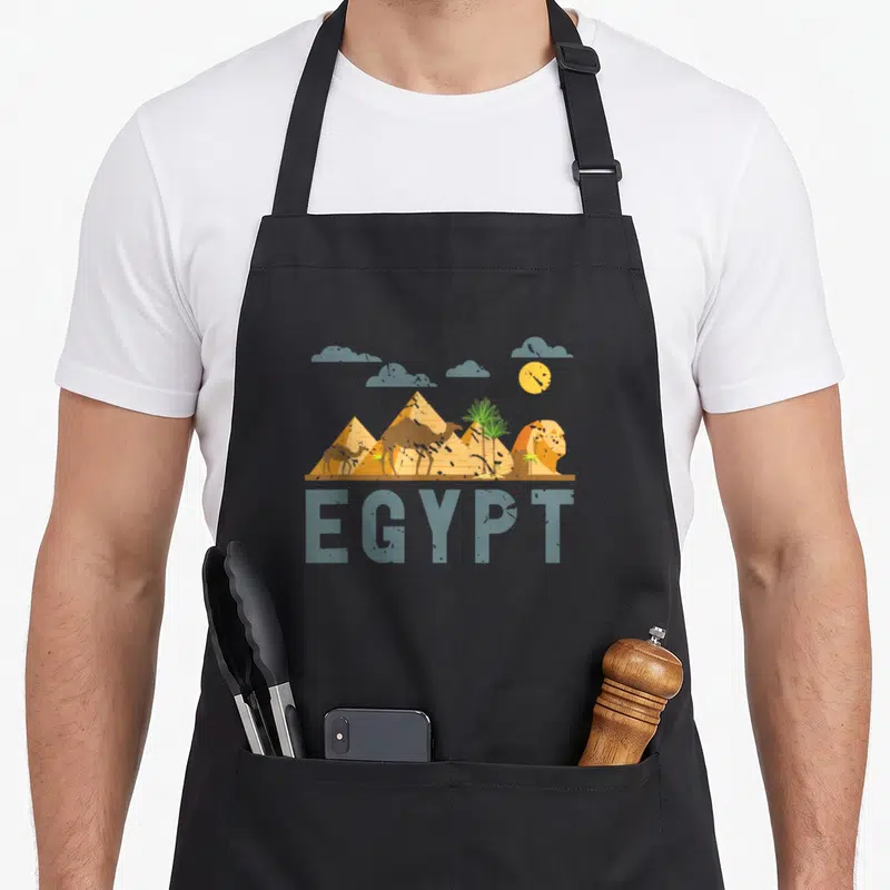 Cairo egyptian apron - Retro Egypt landscape with pyramids camels sphinx and palm trees above EGYPT text — shown on a black cotton canvas apron against a white background