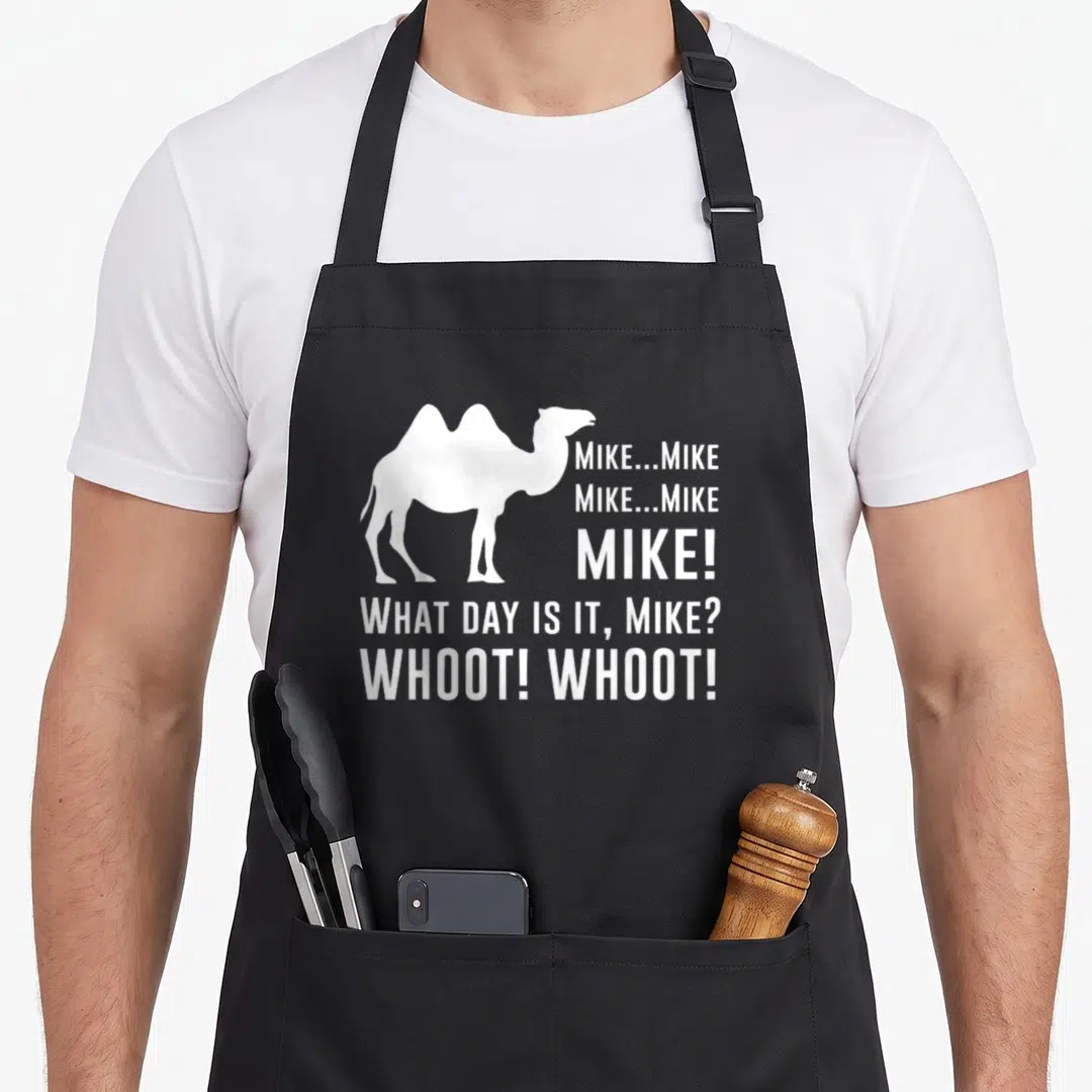 Funny hump camel apron - White camel silhouette next to stacked text reading Mike What Day Is It Whoot Whoot — shown on a black cotton canvas apron against a white background