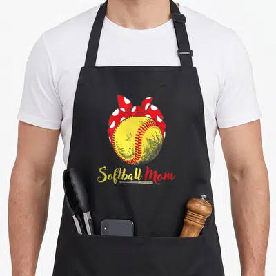 Flag mother's day aprons - Yellow softball with red and white polka dot bow and Softball Mom script text — shown on a black cotton canvas apron against a white background