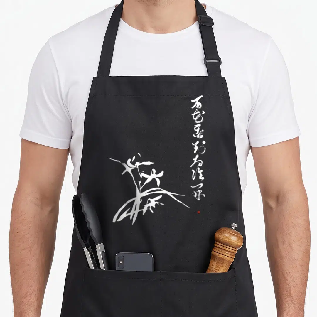 Zen orchid apron - White calligraphic orchid drawing with vertical script and small red stamp on grey background — shown on a black cotton canvas apron against a white background