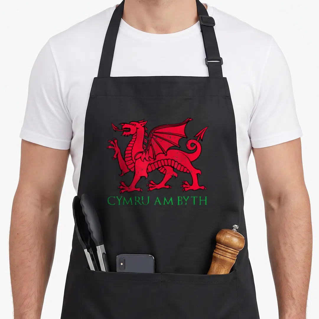 Byth welsh apron - Distressed red dragon centered above green Cymru Am Byth text — shown on a black cotton canvas apron against a white background