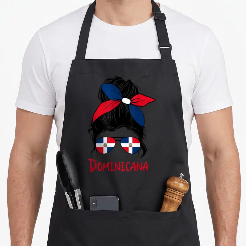 Dominican messy aprons - Woman silhouette with bun, flag sunglasses, and red DOMINICANA text — shown on a black cotton canvas apron against a white background