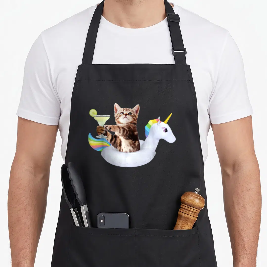 Summer kitty cat apron - Brown tabby kitten in white unicorn float holding margarita with lime slice — shown on a black cotton canvas apron against a white background
