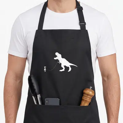 Rex pet apron - White silhouette of a girl holding a leash attached to a large T-Rex dinosaur — shown on a black cotton canvas apron against a white background