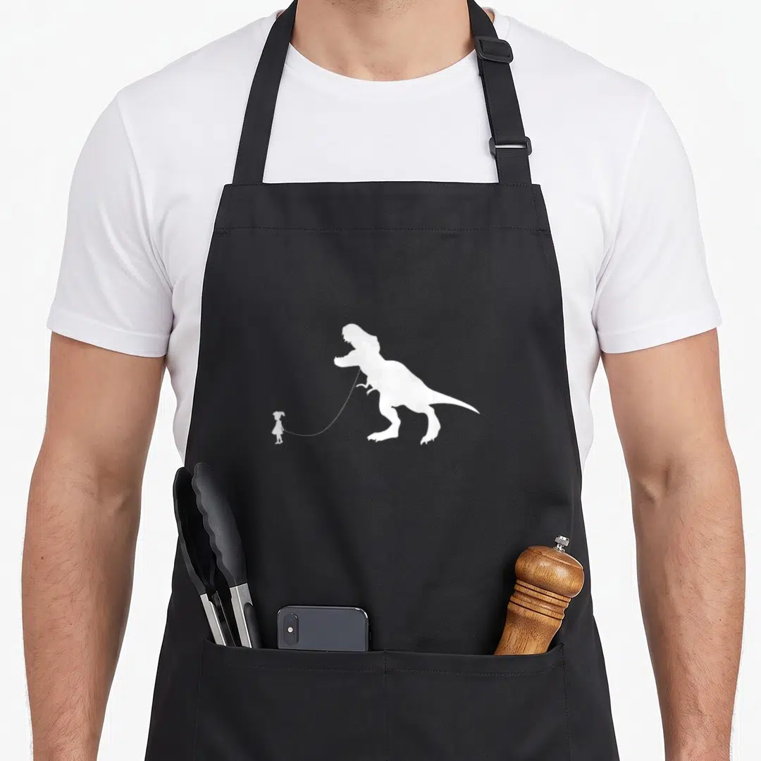 Rex pet apron - White silhouette of a girl holding a leash attached to a large T-Rex dinosaur — shown on a black cotton canvas apron against a white background