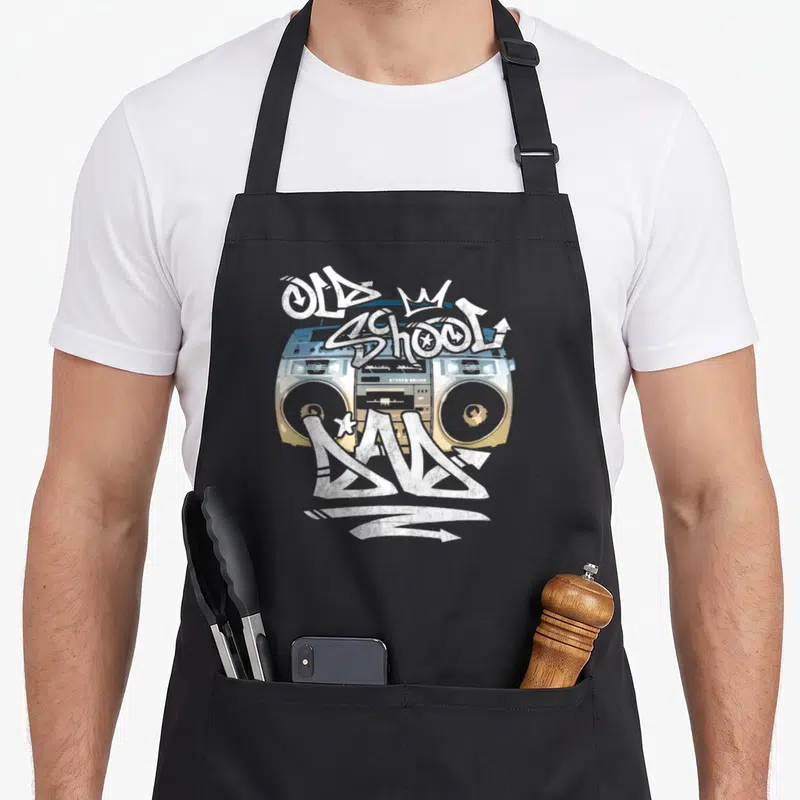 School freestyle dad apron - Cartoon boombox with OLD SCHOOL JAM graffiti text and small crown in blue and yellow — shown on a black cotton canvas apron against a white background