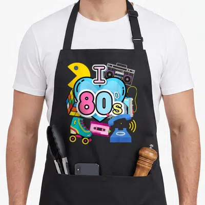 Trip 80s apron - Blue heart with I 80s text surrounded by retro skates, boombox, cassette, phone, and puzzle cube — shown on a black cotton canvas apron against a white background