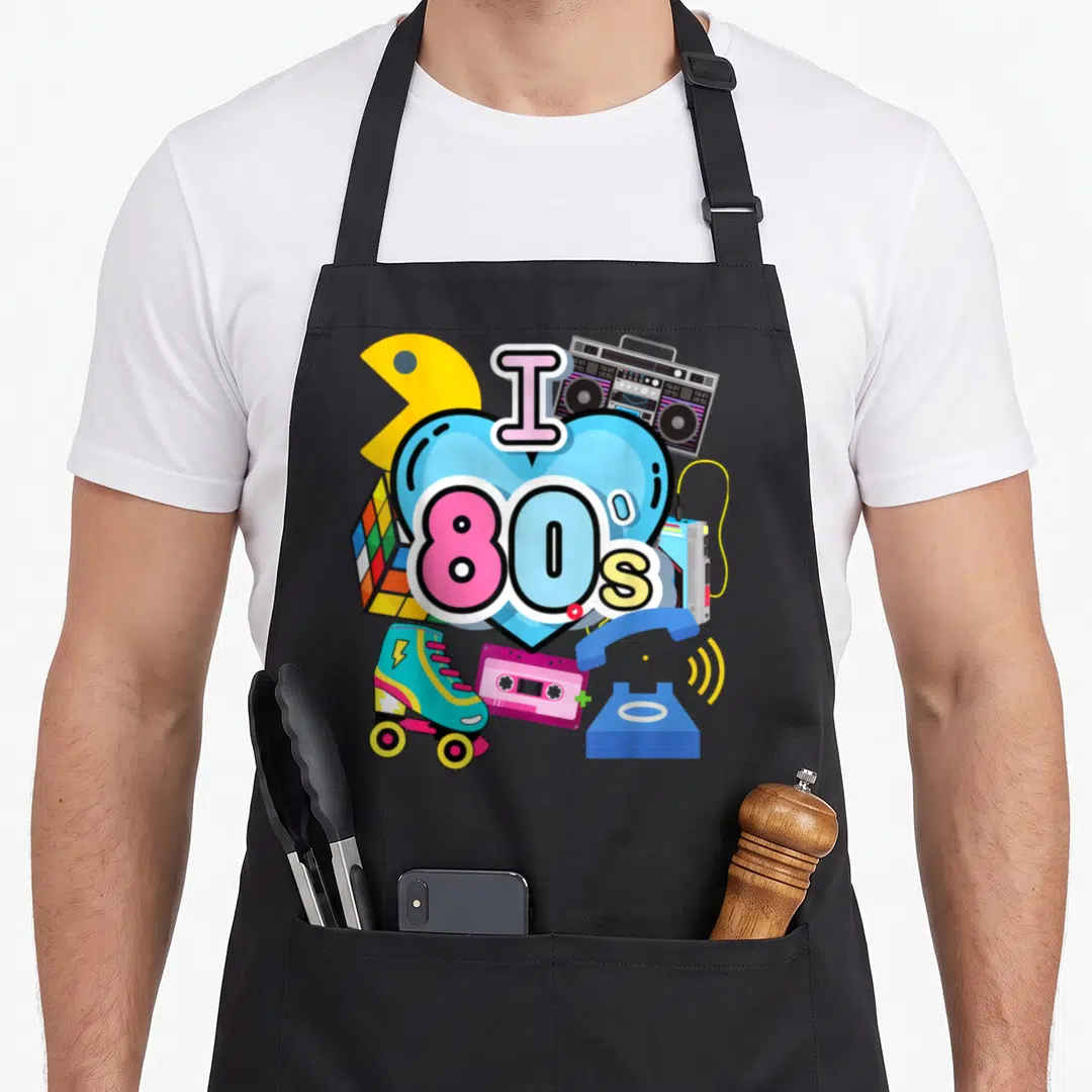 Trip 80s apron - Blue heart with I 80s text surrounded by retro skates, boombox, cassette, phone, and puzzle cube — shown on a black cotton canvas apron against a white background