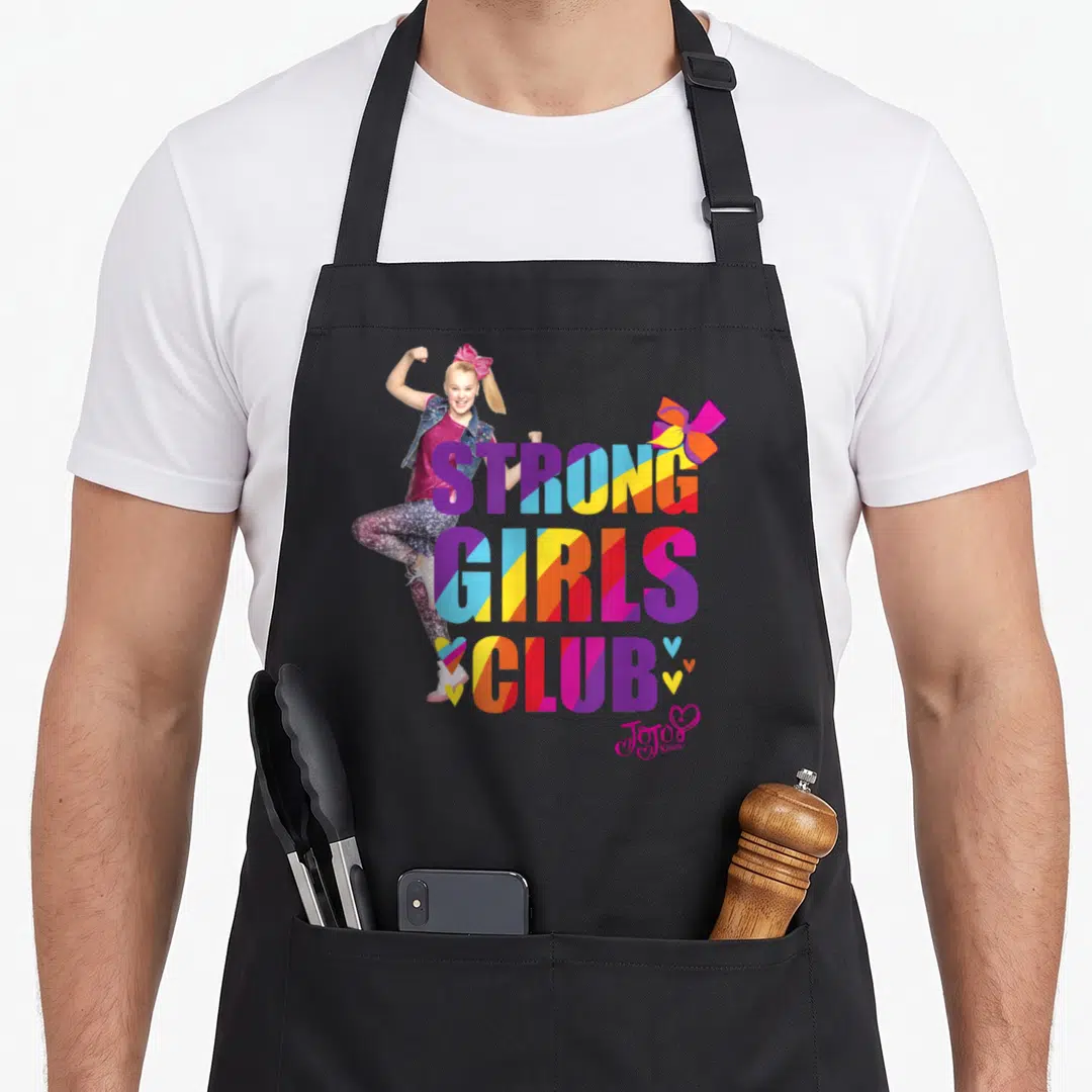 Strong rainbow apron - Girl flexing arm next to multi-colored STRONG GIRLS CLUB text and JoJo Siwa signature — shown on a black cotton canvas apron against a white background
