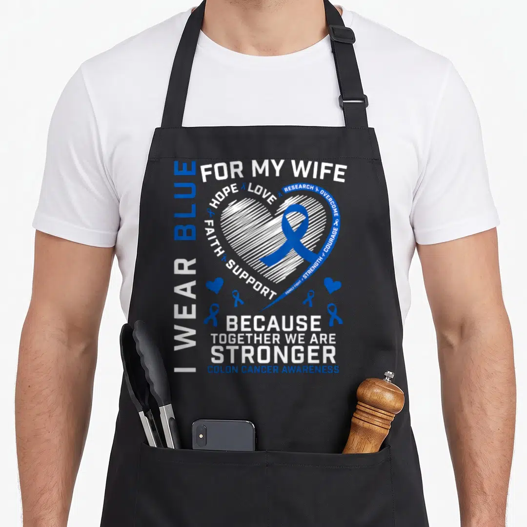 Colon husband wife aprons - White heart with blue ribbon and text I wear blue for my wife colon cancer awareness — shown on a black cotton canvas apron against a white background