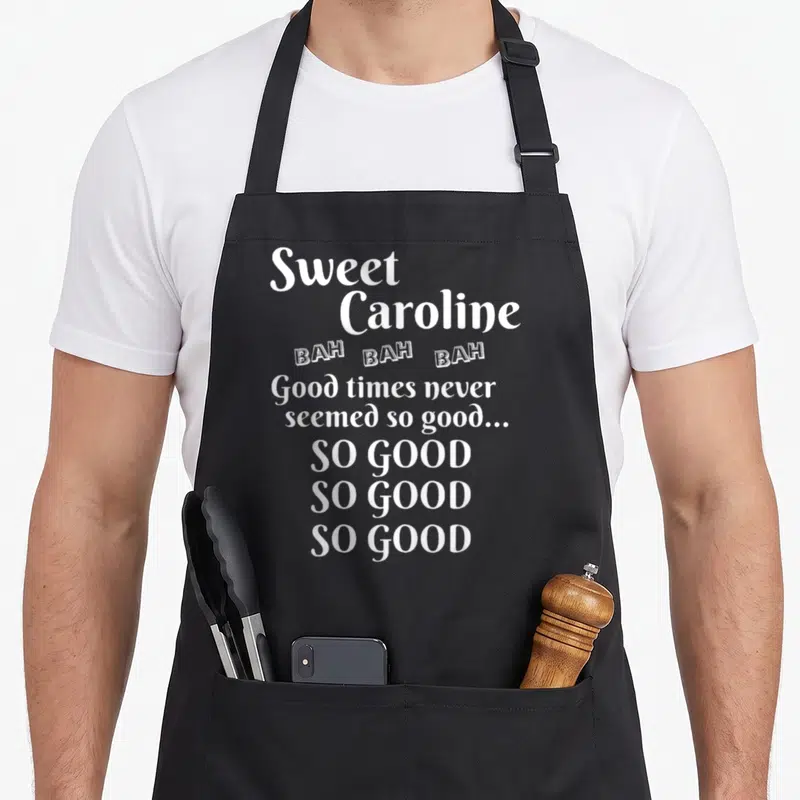 Caroline sweet apron - White stacked text reading Sweet Caroline BAH BAH BAH Good times never seemed so good SO GOOD — shown on a black cotton canvas apron against a white background