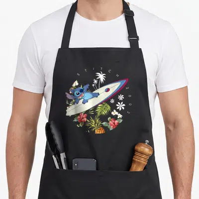 Surfing stitch apron - Blue Stitch lying on surfboard with STITCH 2002 text and tropical flowers — shown on a black cotton canvas apron against a white background