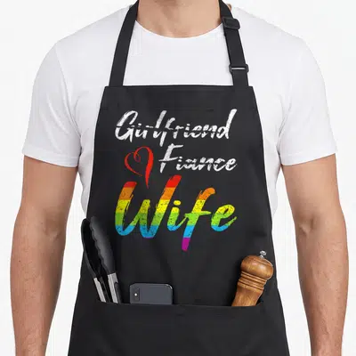 Fiance wife apron - Stacked text Girlfriend Fiance Wife with red heart and rainbow stripes — shown on a black cotton canvas apron against a white background