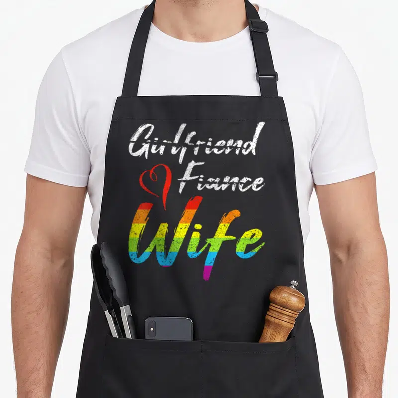 Fiance wife apron - Stacked text Girlfriend Fiance Wife with red heart and rainbow stripes — shown on a black cotton canvas apron against a white background