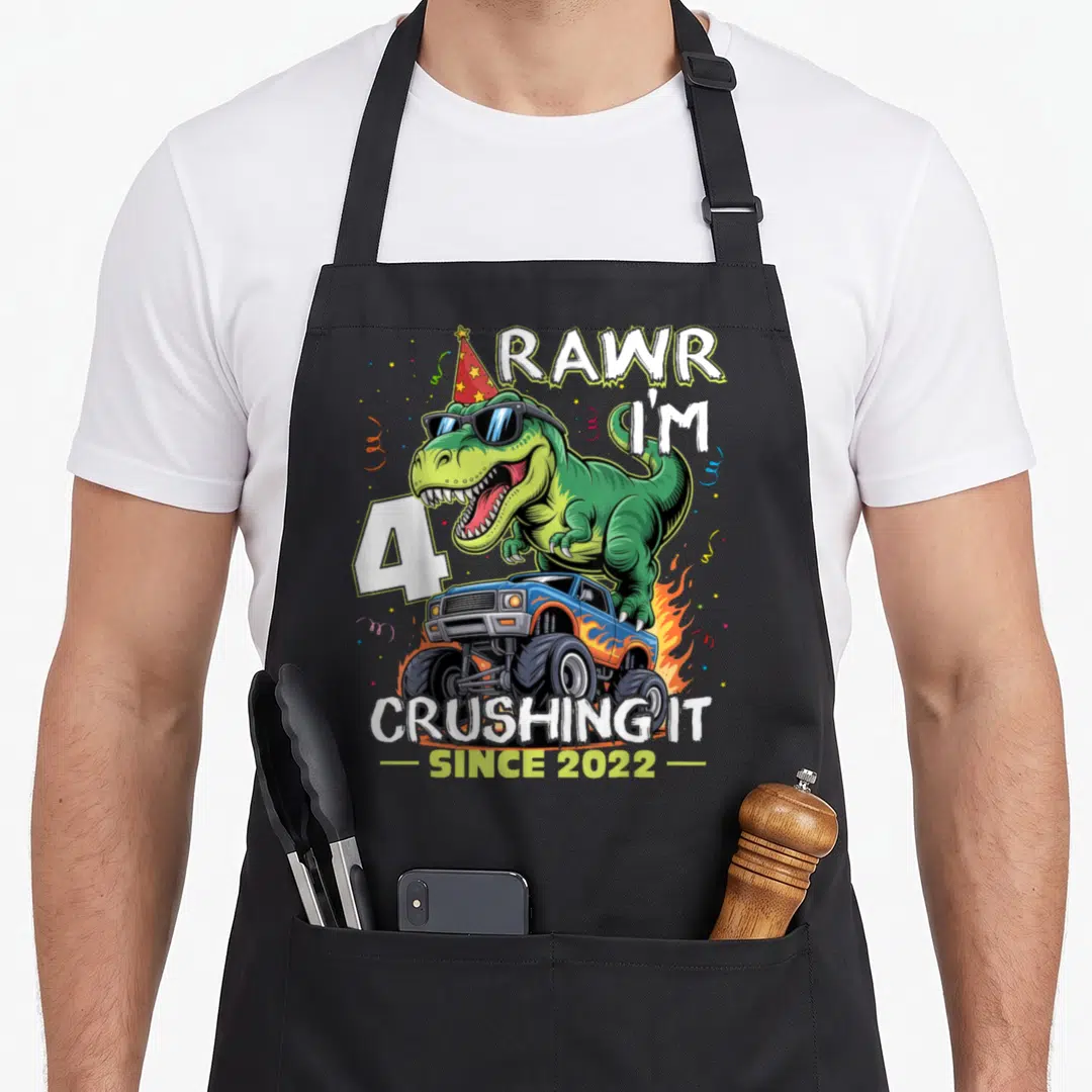 4th birthday monster truck apron - T-Rex in sunglasses and party hat on blue monster truck with celebratory text — shown on a black cotton canvas apron against a white background
