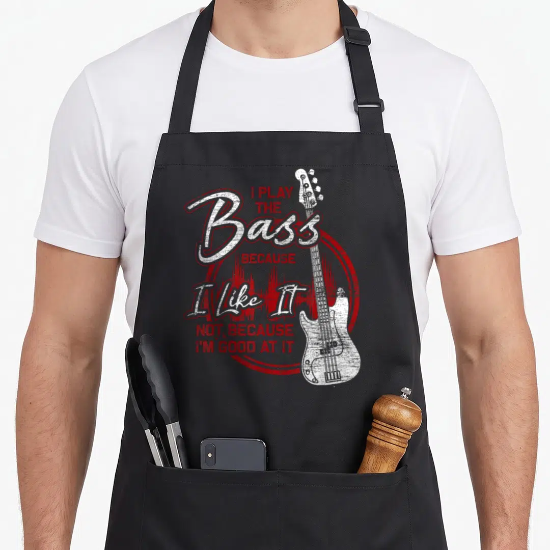 Bass guitar bassist apron - White distressed bass guitar on red circle with I Play The Bass Because I Like It text — shown on a black cotton canvas apron against a white background