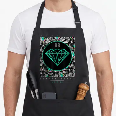 Venice floral apron - Cyan diamond and 98 in circle over tropical leaves with Venice Beach text — shown on a black cotton canvas apron against a white background