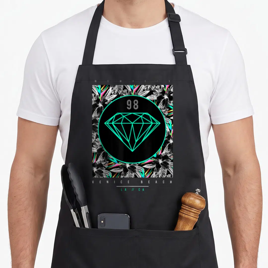 Venice floral apron - Cyan diamond and 98 in circle over tropical leaves with Venice Beach text — shown on a black cotton canvas apron against a white background