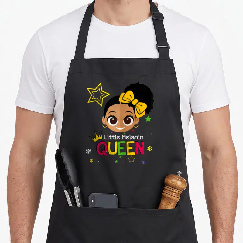 Melanin queen apron - Cartoon girl with yellow bow and crown, text Little Melanin QUEEN surrounded by stars — shown on a black cotton canvas apron against a white background