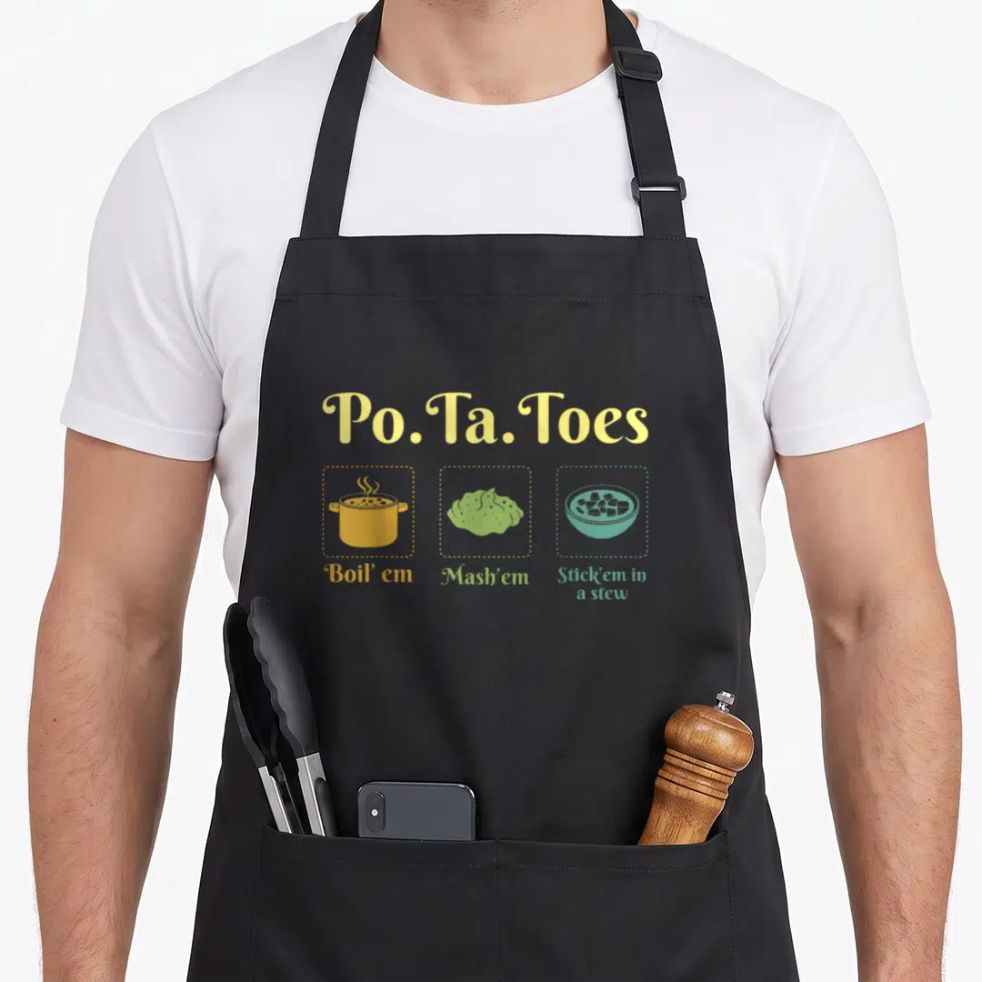 Toe potato apron - Cartoon potatoes in yellow pot, green mash, teal stew bowl with rhyming text — shown on a black cotton canvas apron against a white background