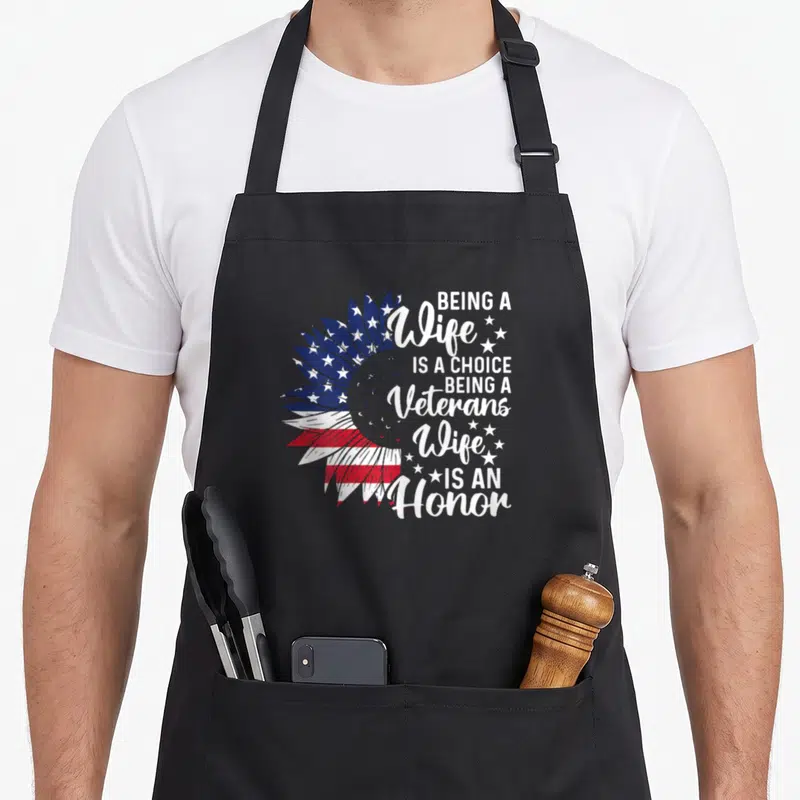 Honor patriotic apron - Sunflower with red white and blue flag pattern and stacked text about veterans wife honor — shown on a black cotton canvas apron against a white background