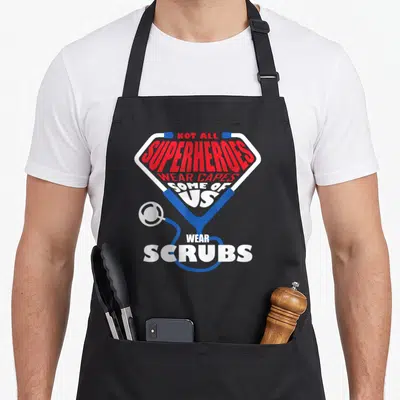 Heroe cape nurse apron - Stethoscope forming diamond shape around red and white text about superheroes wearing scrubs — shown on a black cotton canvas apron against a white background