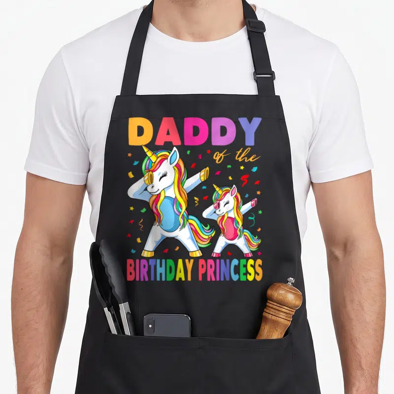 Birthday dabbing unicorn princess apron - Two dabbing unicorns with rainbow hair under DADDY of the BIRTHDAY PRINCESS — shown on a black cotton canvas apron against a white background