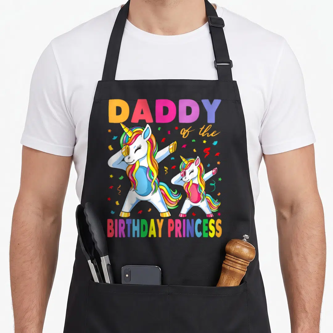 Birthday dabbing unicorn princess apron - Two dabbing unicorns with rainbow hair under DADDY of the BIRTHDAY PRINCESS — shown on a black cotton canvas apron against a white background