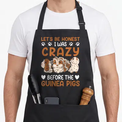 Rodent crazy guinea lady apron - Stacked text reading Let's Be Honest I Was Crazy Before The Guinea Pigs above three — shown on a black cotton canvas apron against a white background
