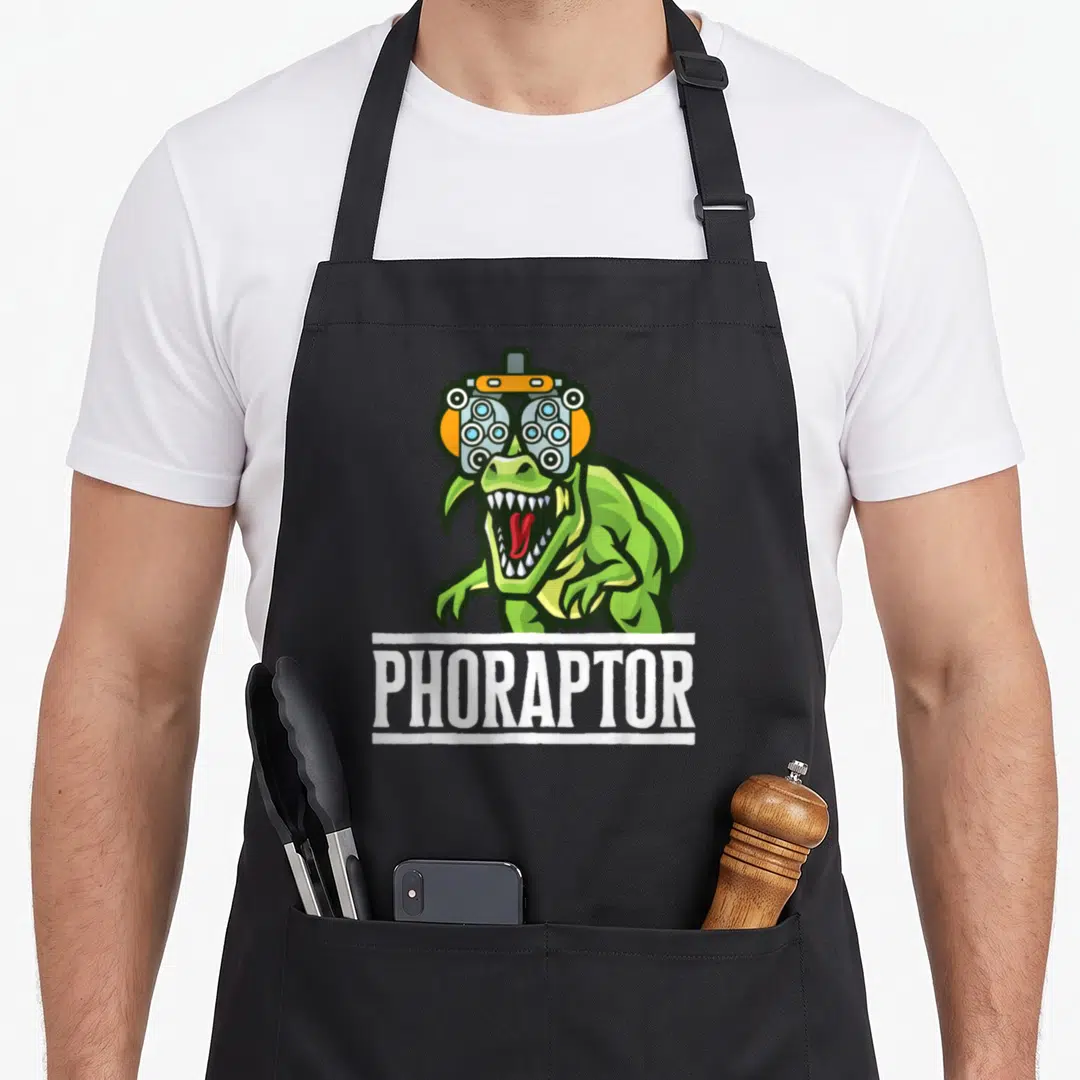 Optometry machine apron - Green dinosaur wearing a phoropter with white PHORAPTOR text banner below — shown on a black cotton canvas apron against a white background