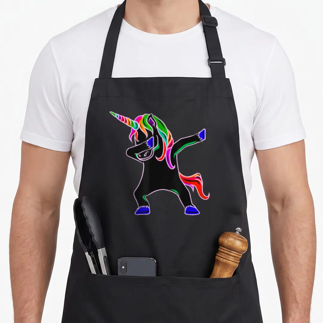 Edm unicorn apron - Black cartoon unicorn dabbing with rainbow mane and tail in pink blue green orange — shown on a black cotton canvas apron against a white background