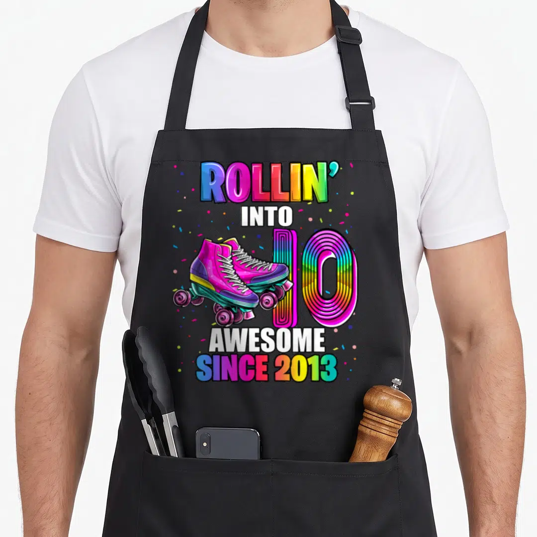Skating 10th birthday apron - Rollin into 10 Awesome since 2013 roller skates rainbow text confetti — shown on a black cotton canvas apron against a white background
