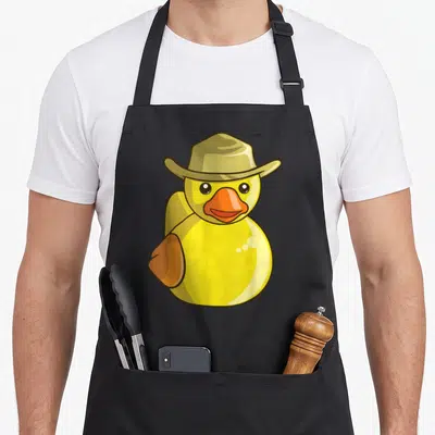 Cowboy cotton duck apron - Yellow cartoon rubber duck wearing an olive cowboy hat with an orange beak — shown on a black cotton canvas apron against a white background