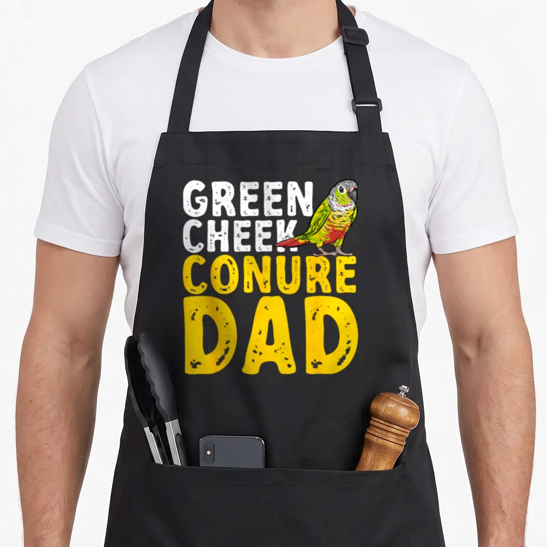 Cheek conure bird apron - Stacked Green Cheek Conure Dad text with cartoon parrot in green yellow and red — shown on a black cotton canvas apron against a white background