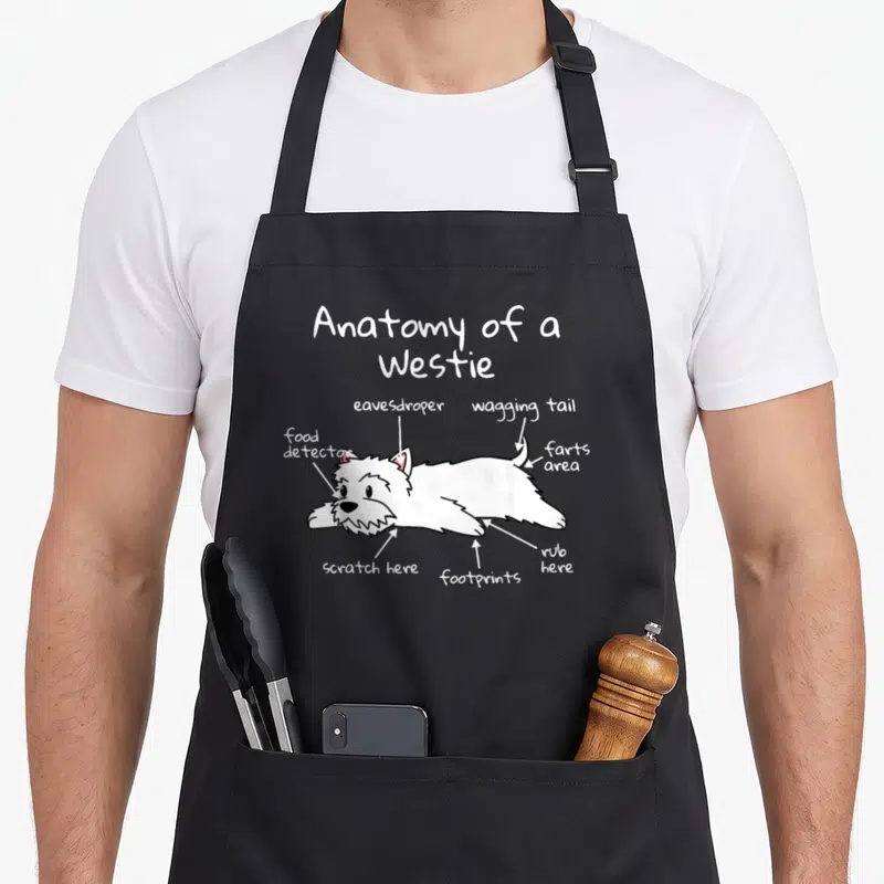 Anatomy westie apron - Cartoon white Westie labeled with eavesdroper, food detector, and farts area text — shown on a black cotton canvas apron against a white background