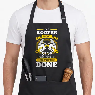 Roofer mechanic apron - Crossed hammers in shield with I'm A Roofer I Don't Stop When I'm Tired I Stop When I'm Done — shown on a black cotton canvas apron against a white background