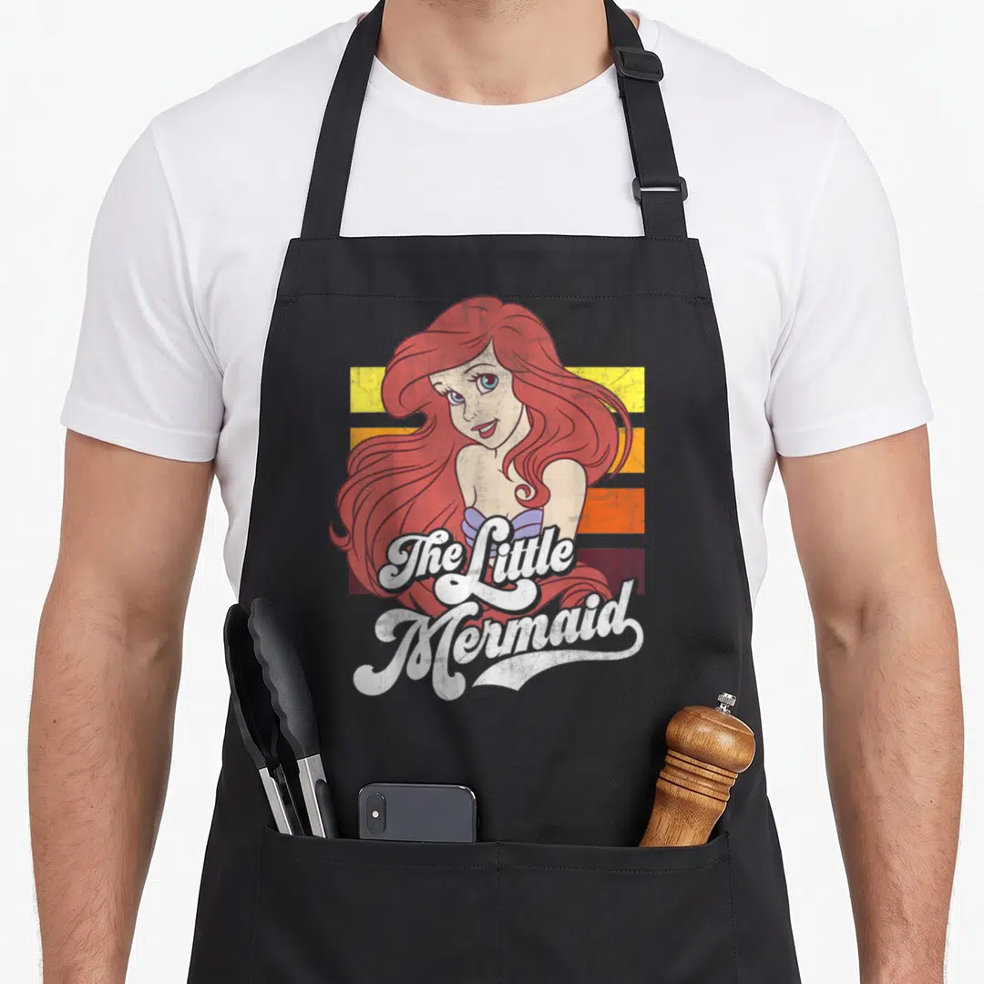 Cute stripe apron - Cartoon mermaid with red hair on red yellow orange and purple stripes with white script text — shown on a black cotton canvas apron against a white background
