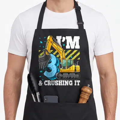 Excavator 3rd construction apron - Yellow excavator crushing blue number 3 with white text and caution stripes — shown on a black cotton canvas apron against a white background