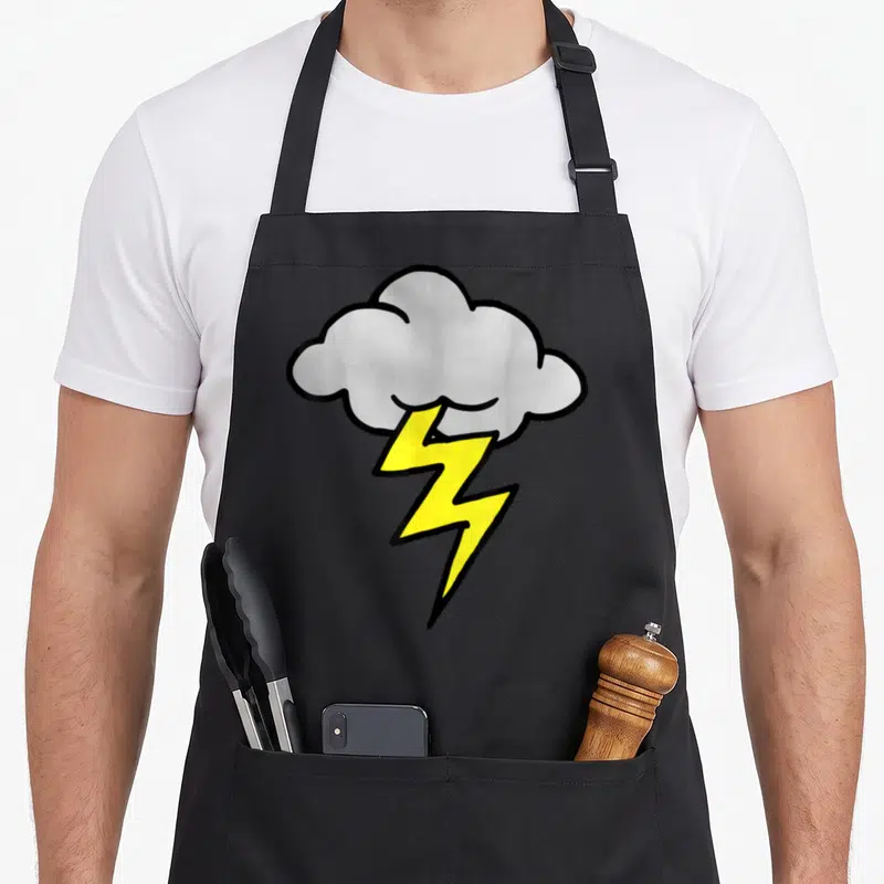 Bolt thunder apron - Cartoon yellow lightning bolt striking down from a grey cloud with thick black outlines — shown on a black cotton canvas apron against a white background