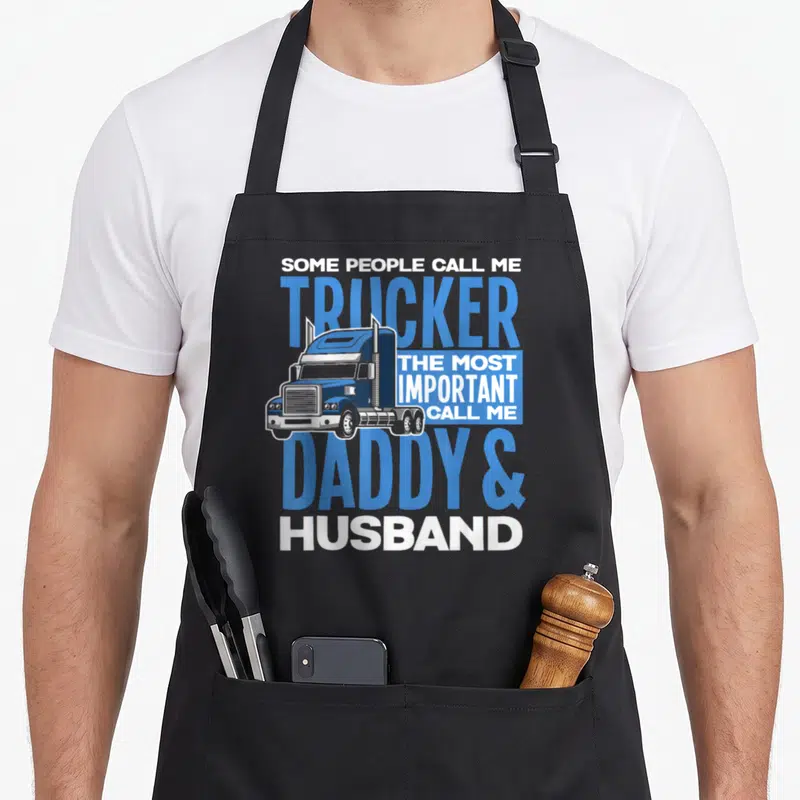 Trucker driving aprons - Semi-truck graphic with blue and white text reading Trucker Daddy Husband — shown on a black cotton canvas apron against a white background