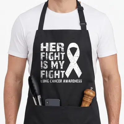 Fight lungs apron - White distressed text reading Her Fight Is My Fight next to a large white awareness ribbon — shown on a black cotton canvas apron against a white background